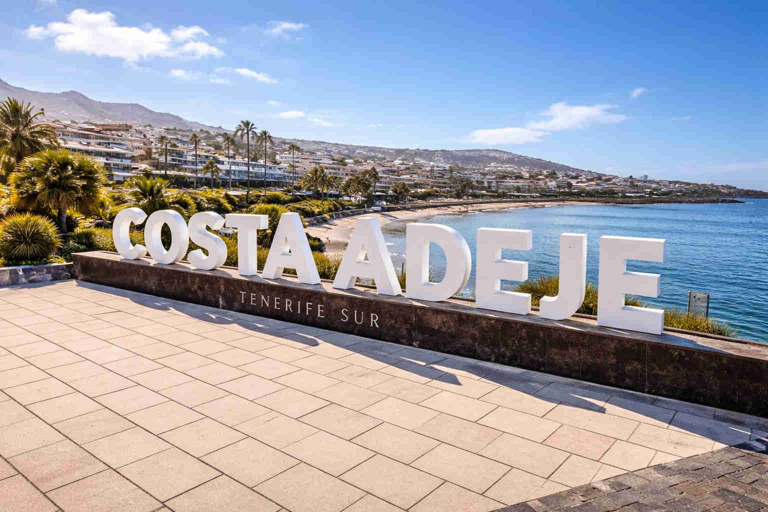 Letrero de Costa Adeje con vista al paseo marítimo, playa y costa del sur de Tenerife en un día soleado