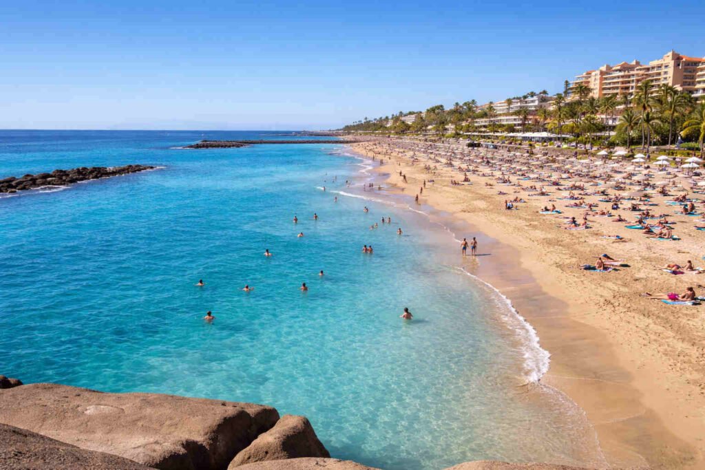 Playa de Costa Adeje en Tenerife con arena dorada, mar tranquilo y turistas disfrutando del sol