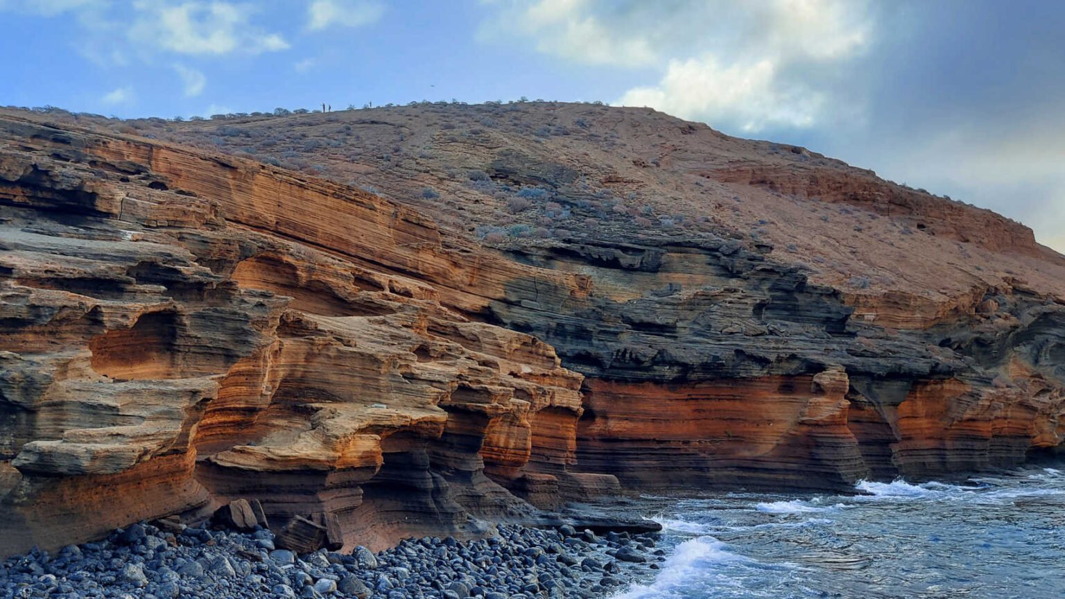 Formaciones rocosas volcánicas en el Monumento Natural de Montaña Amarilla en Tenerife junto al mar, con capas de colores y costa salvaje