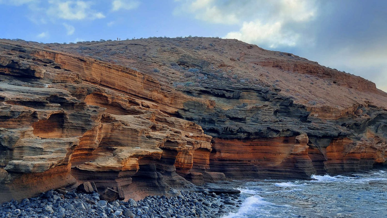 Formaciones rocosas volcánicas en el Monumento Natural de Montaña Amarilla en Tenerife junto al mar, con capas de colores y costa salvaje