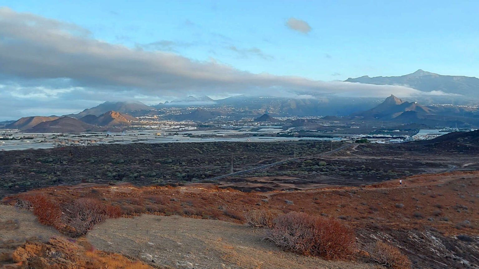 Vista del sur de Tenerife desde Montaña Amarilla con paisaje volcánico, invernaderos y montañas al fondo