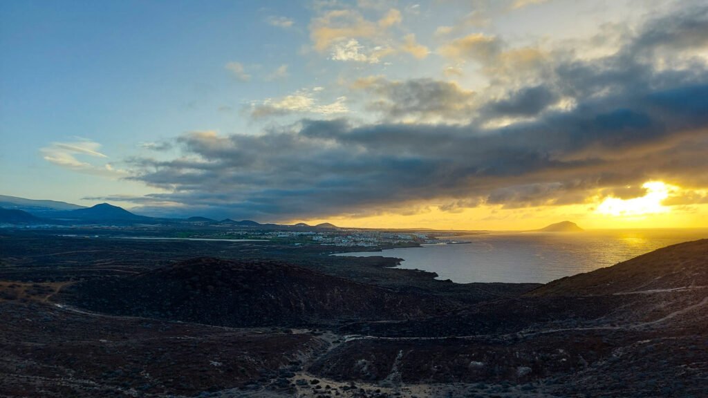 Panorámica del sur de Tenerife desde Montaña Amarilla al atardecer, con costa volcánica, núcleo urbano y el océano