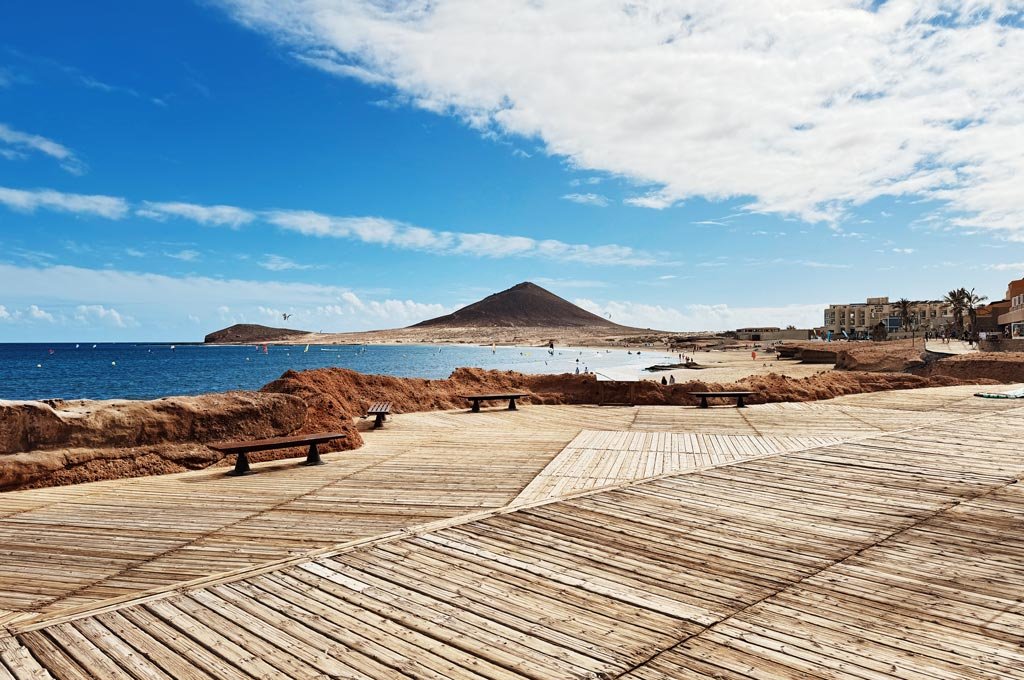 Paseo marítimo de El Médano con tarimas de madera, costa volcánica y Montaña Roja al fondo, en el sur de Tenerife