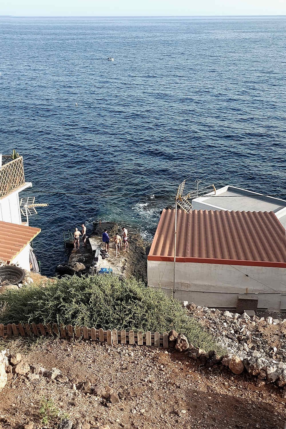 Zona de baño en Bocacangrejo, Tenerife, con personas junto a una plataforma de roca volcánica al borde del mar Atlántico.