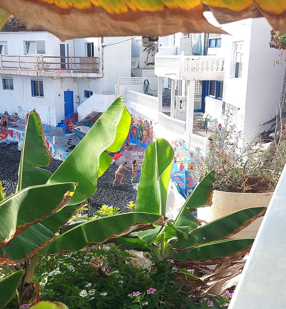 Vista interior de Bocacangrejo, en Tenerife, con casas blancas del pueblo y personas disfrutando de una pequeña cala entre vegetación tropical.