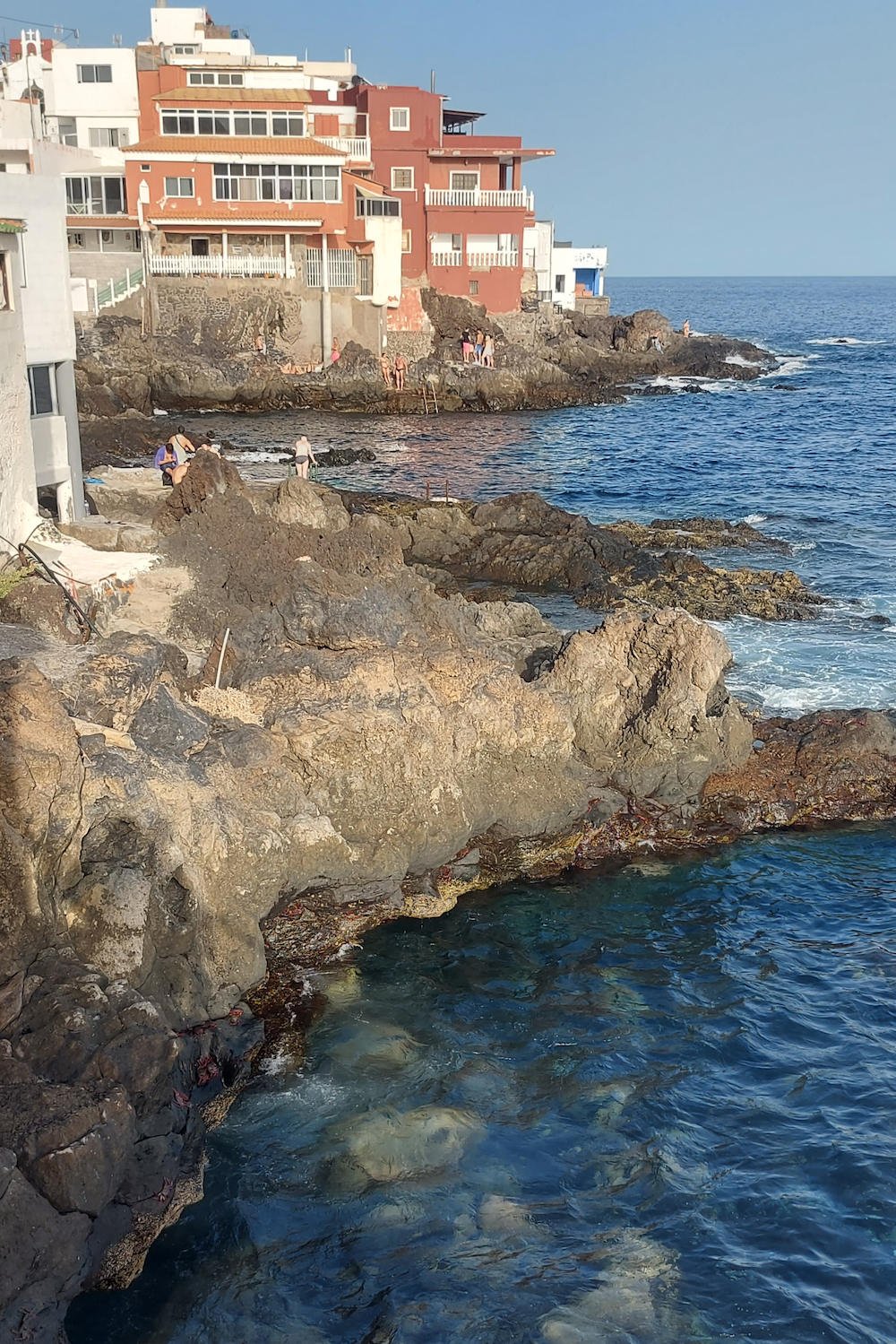 Costa rocosa de Bocacangrejo, en Tenerife, con casas del pueblo junto al mar Atlántico y zonas naturales de baño entre lava volcánica.con viviendas sobre roca volcánica y personas bañándose