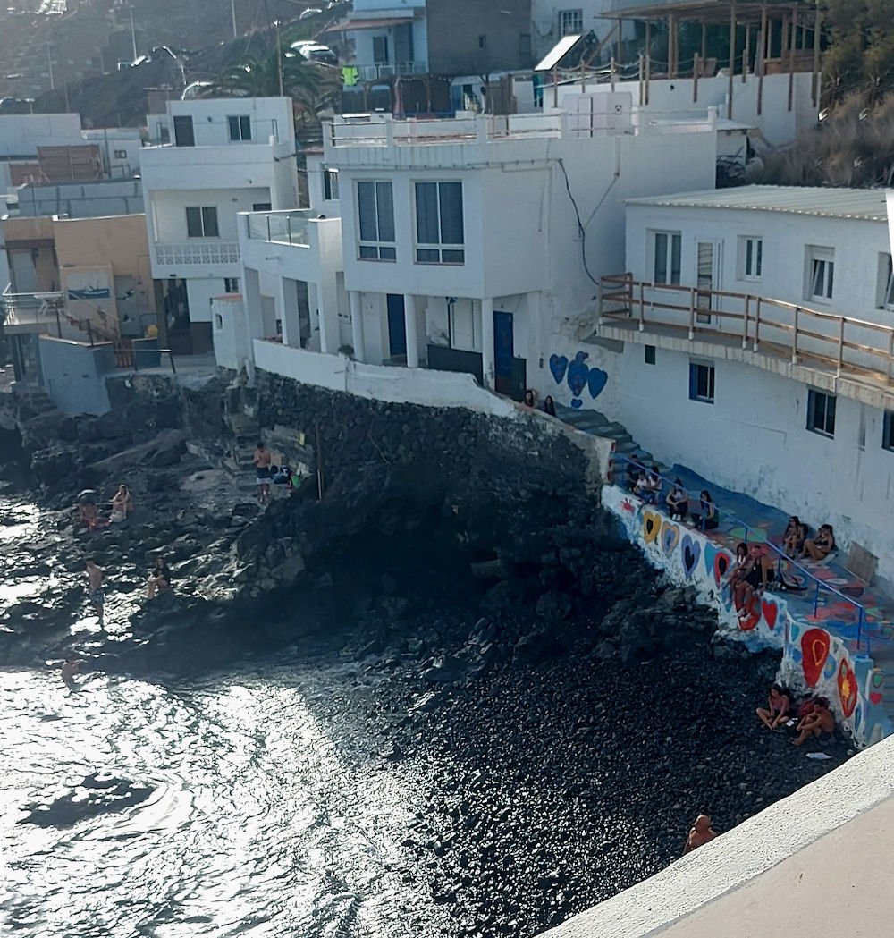 Vista interior de Bocacangrejo, en Tenerife, con casas blancas del pueblo y personas disfrutando de una pequeña cala entre vegetación tropical.